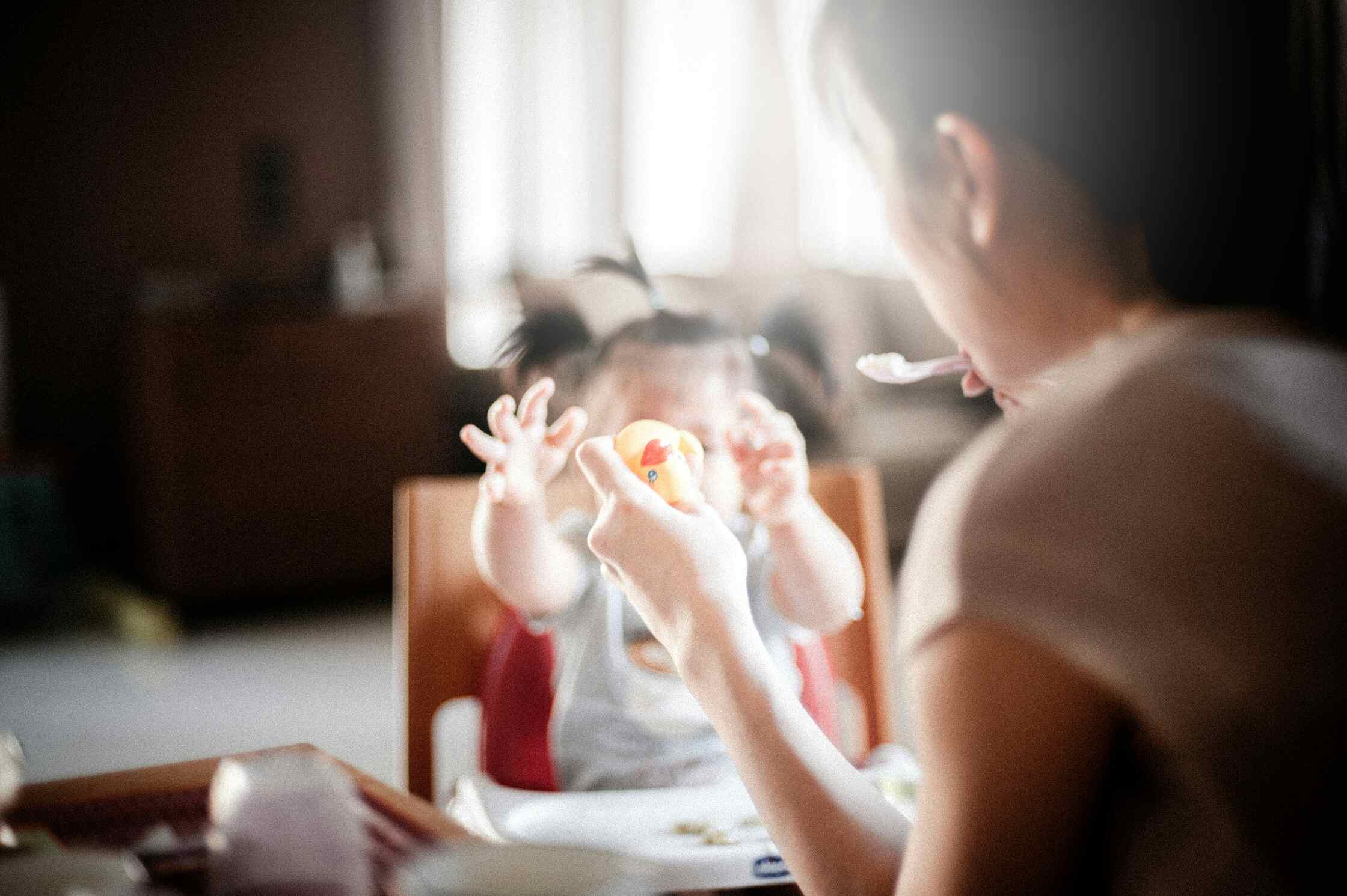 Bé ngồi ghế ăn dặm tự cầm nắm thức ăn và tự lập ăn uống.