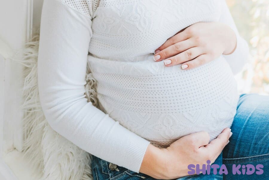 Bà bầu bị phù chân ngồi nghỉ ngơi, giữ bụng nhẹ nhàng trong không gian sáng thoáng